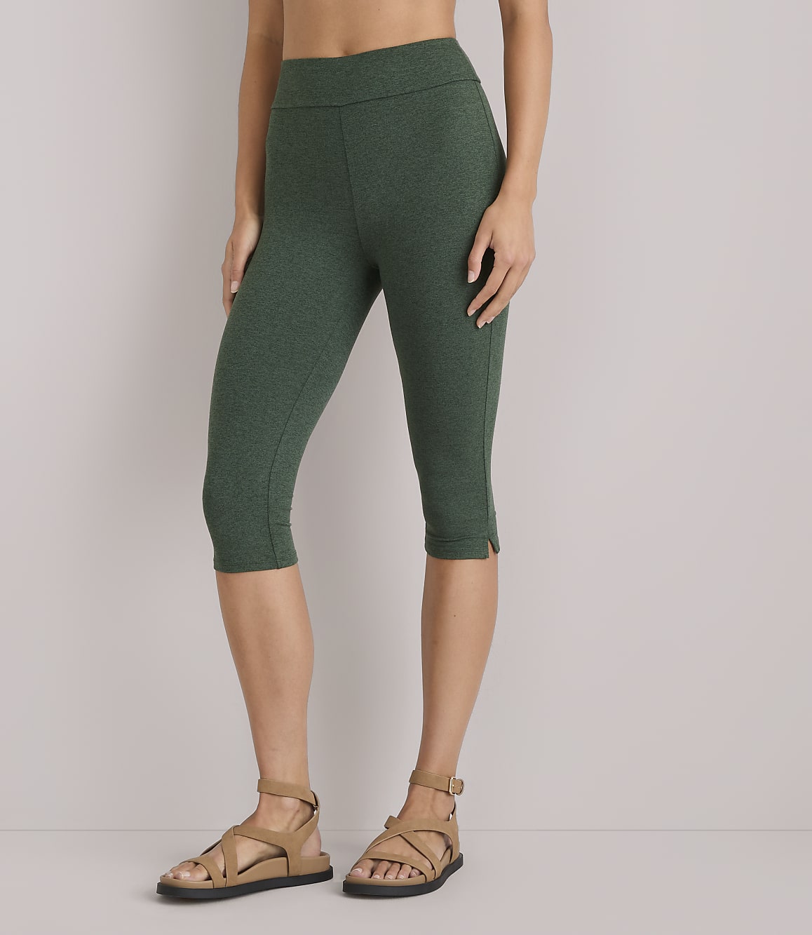 A woman in green capri leggings and brown sandals stands against a plain white background.