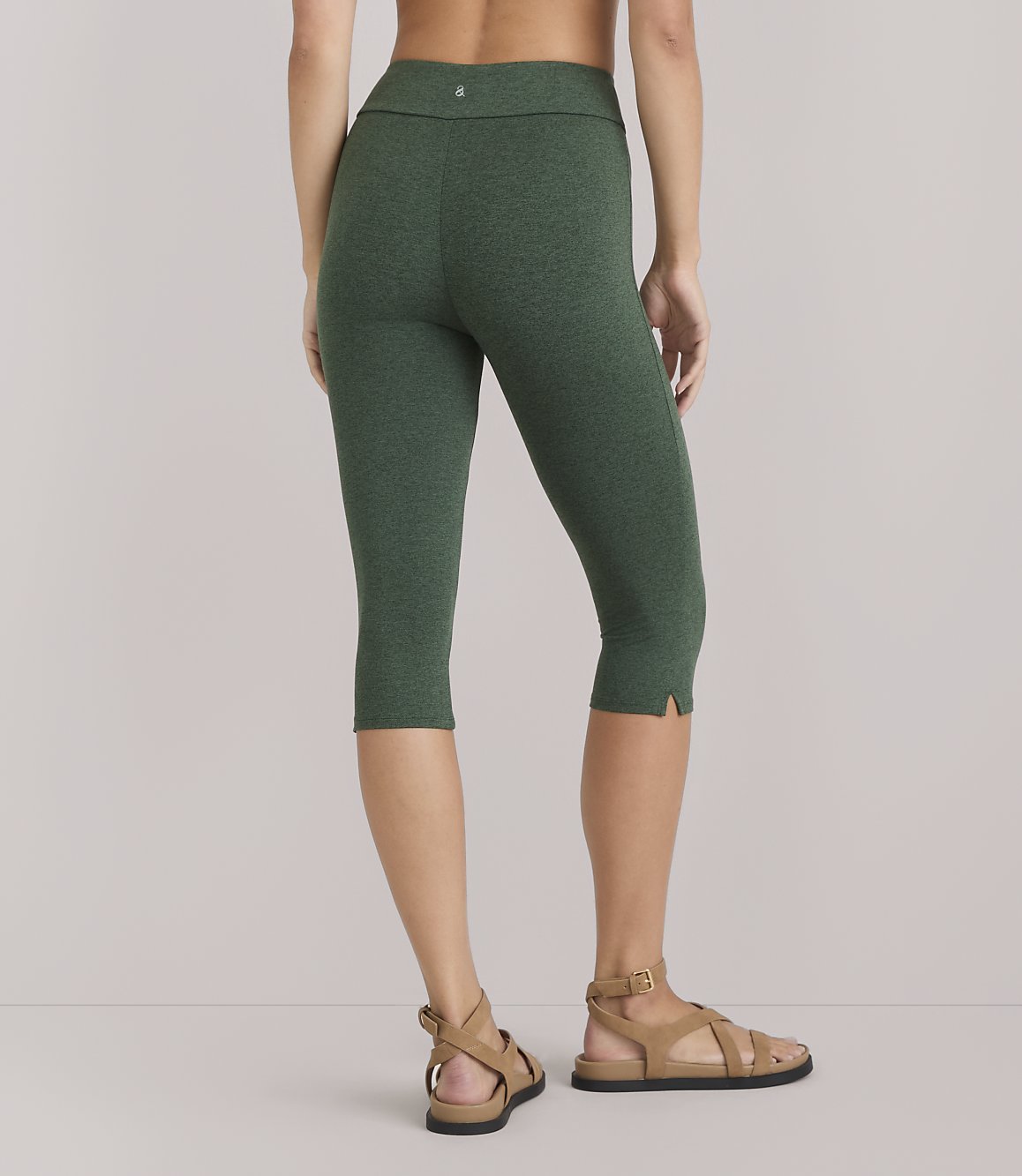 A woman in green capri leggings and sandals stands against a plain white background.
