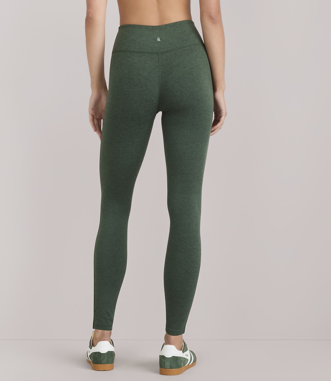 A woman wearing green heathered leggings and white-and-green sneakers stands against a plain white background.