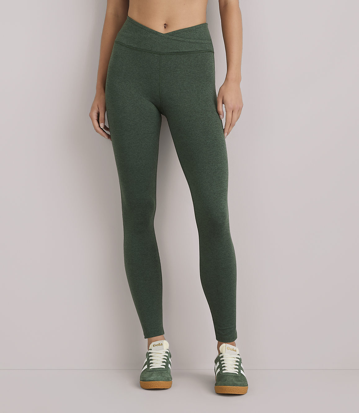 A person wearing green heathered leggings and green sneakers stands against a plain white background.