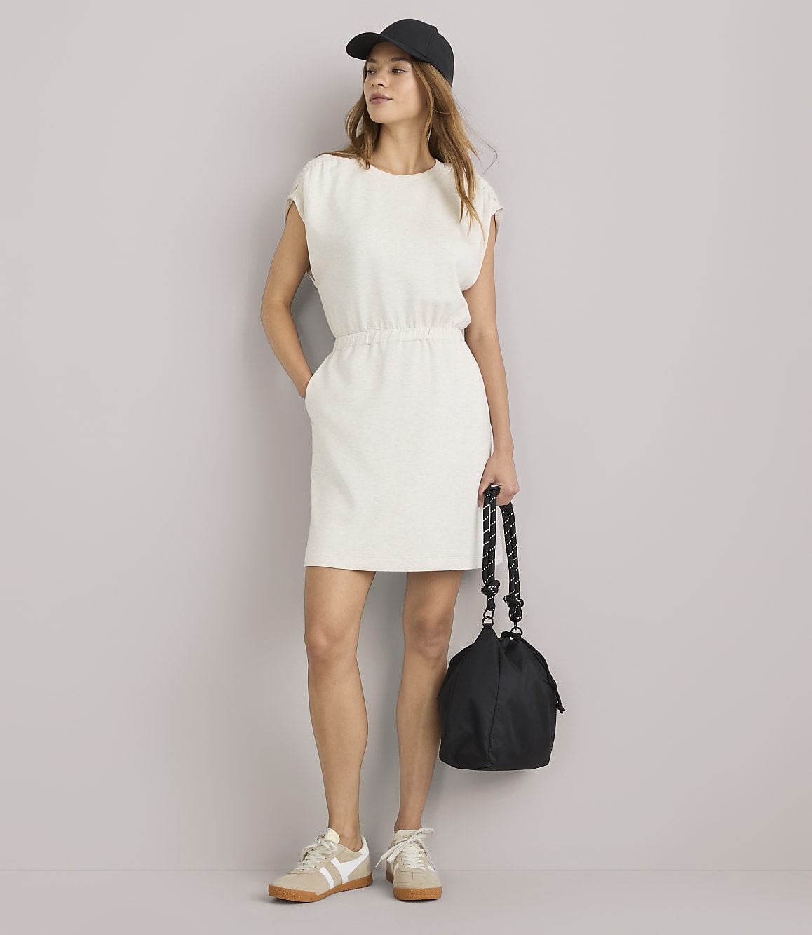A young woman in a cream-colored dress stands against a plain white background.