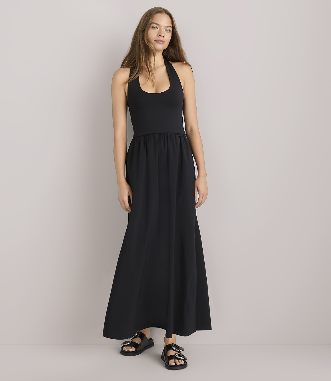 A woman in a black halter dress and a green striped shirt sits against a plain white background.