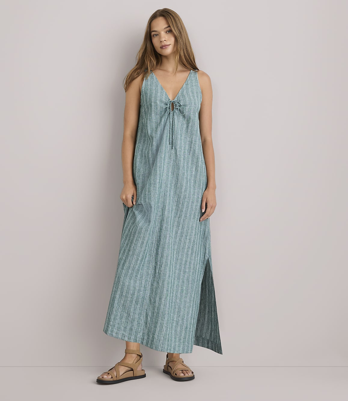 A young woman in a green striped dress stands with her arms crossed against a plain white background.