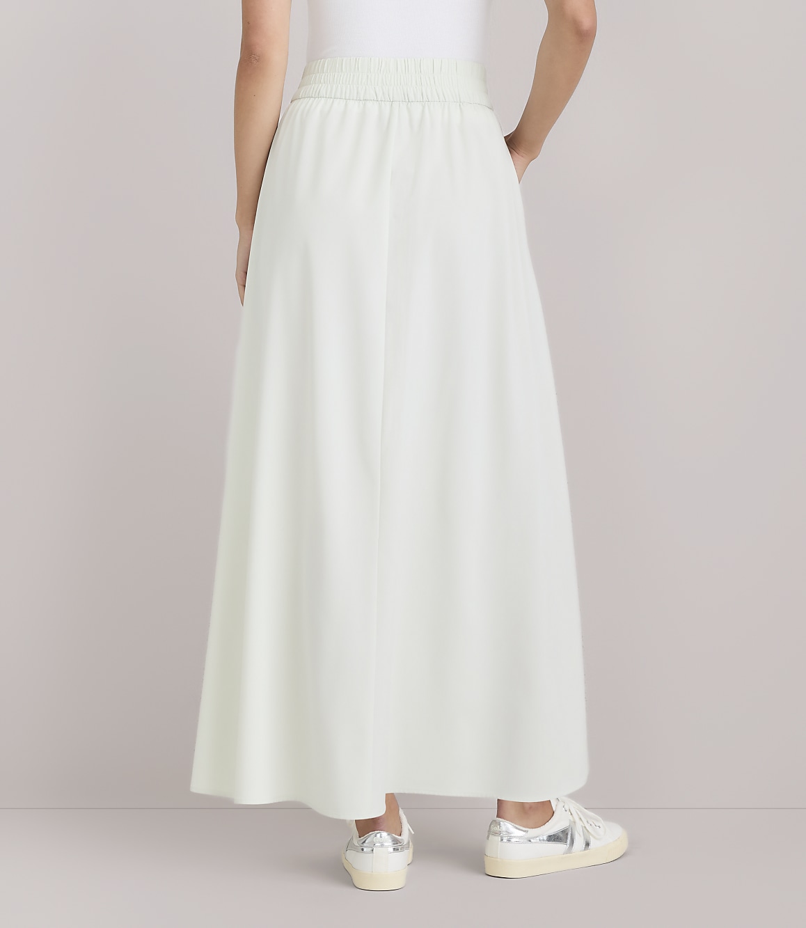 A person wearing a light green maxi skirt and sneakers stands against a plain white background.