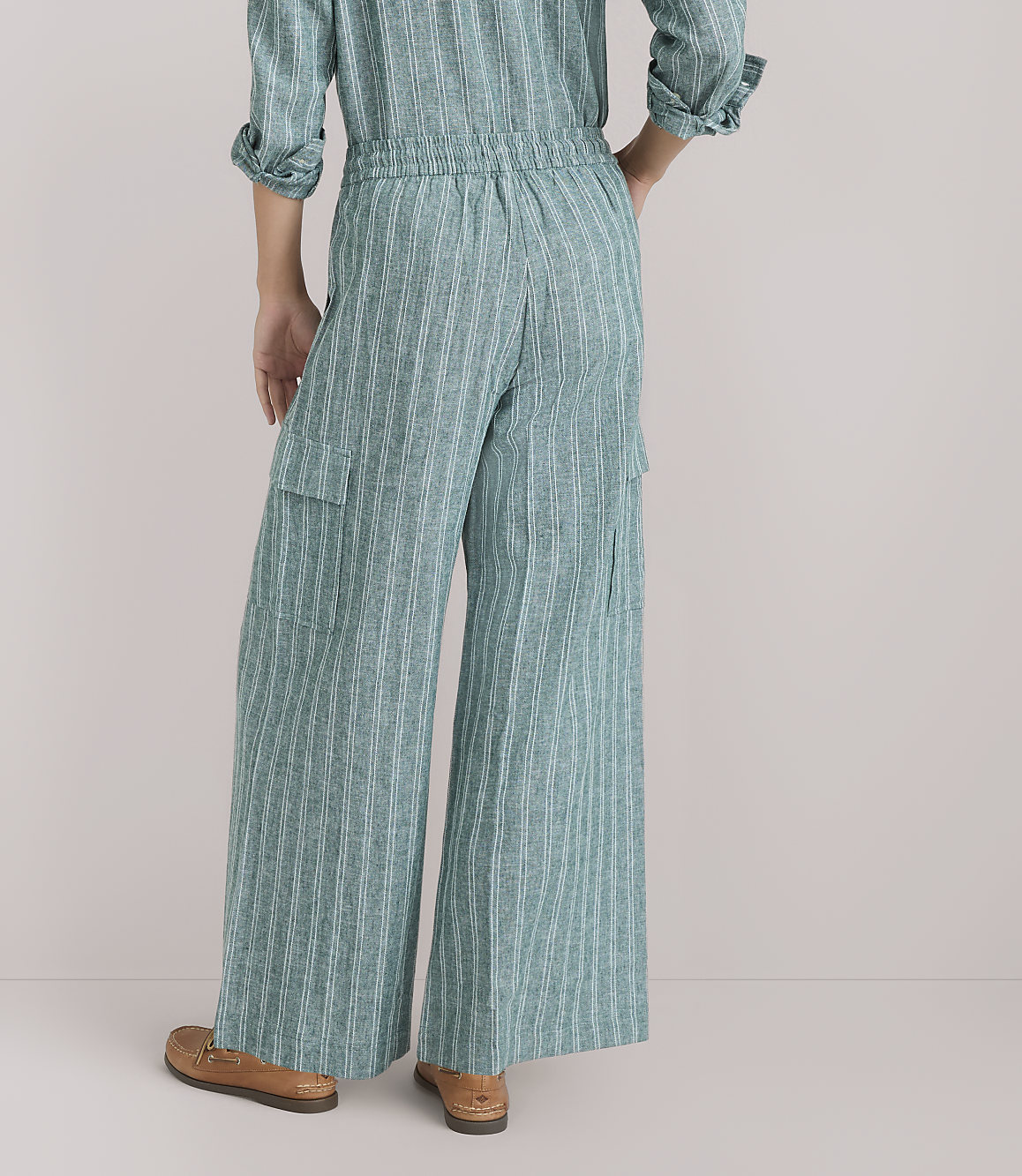 A person wearing a green striped jumpsuit and brown loafers stands against a plain white background.