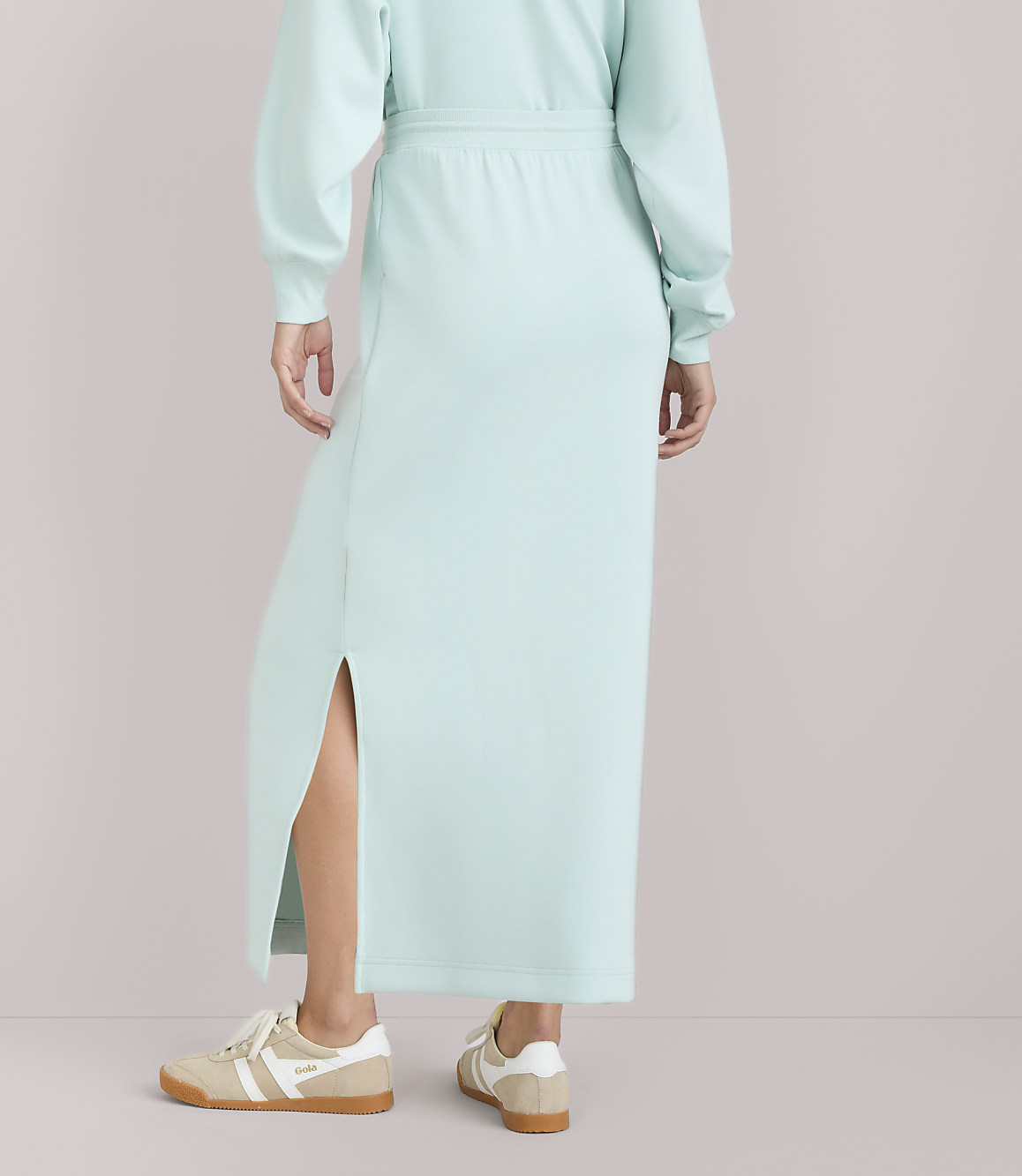 A person wearing a light blue dress and sneakers stands against a plain white background.