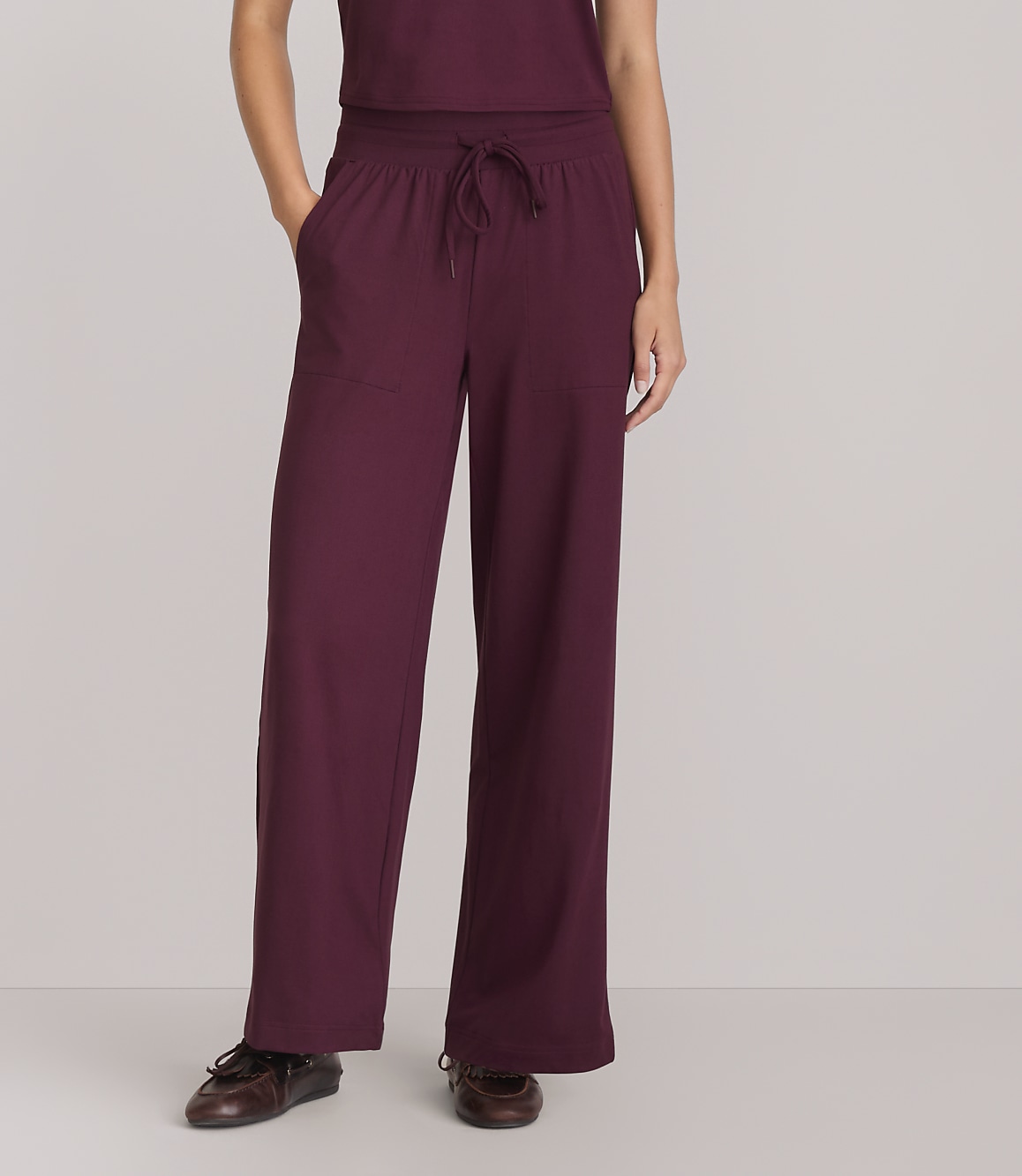 A person wearing maroon wide-leg pants and brown shoes stands against a plain gray background.