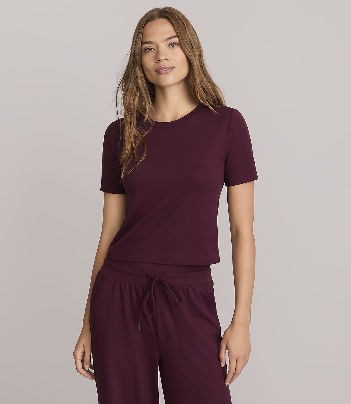 A woman in a maroon t-shirt and matching pants stands against a plain gray background.