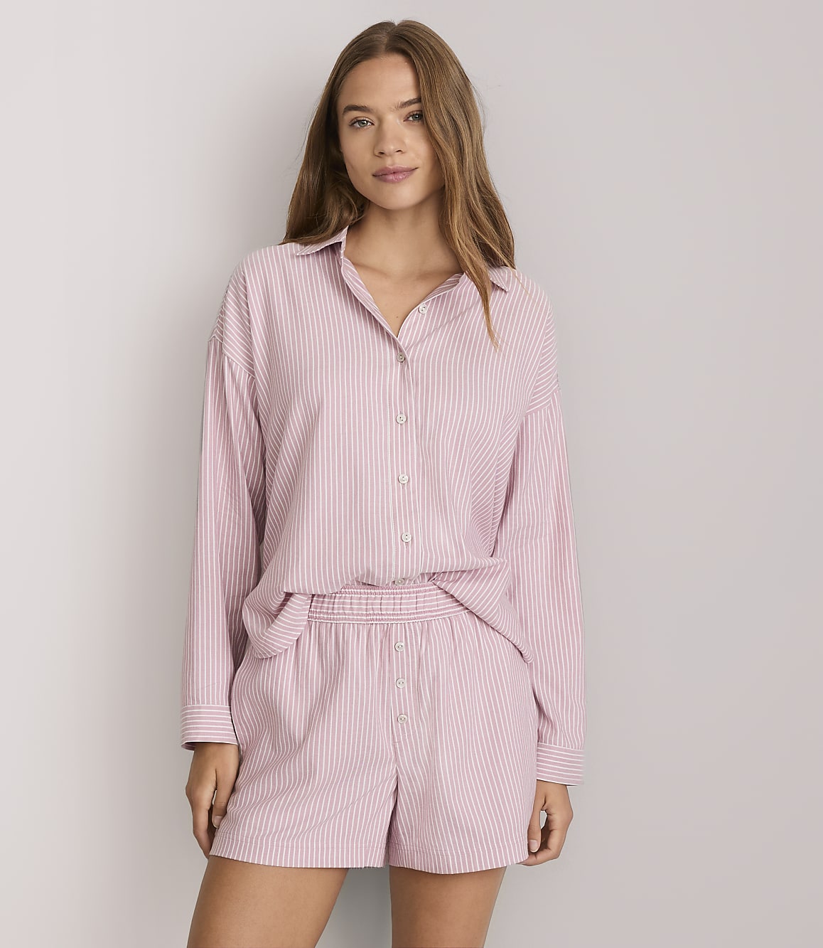 A woman in pink and white striped pajamas stands against a plain white background.