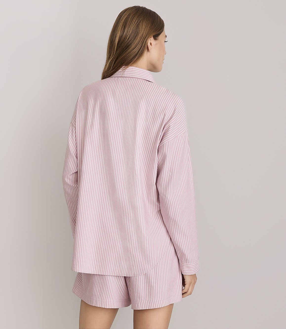 A woman in pink and white striped pajamas stands against a plain white background.