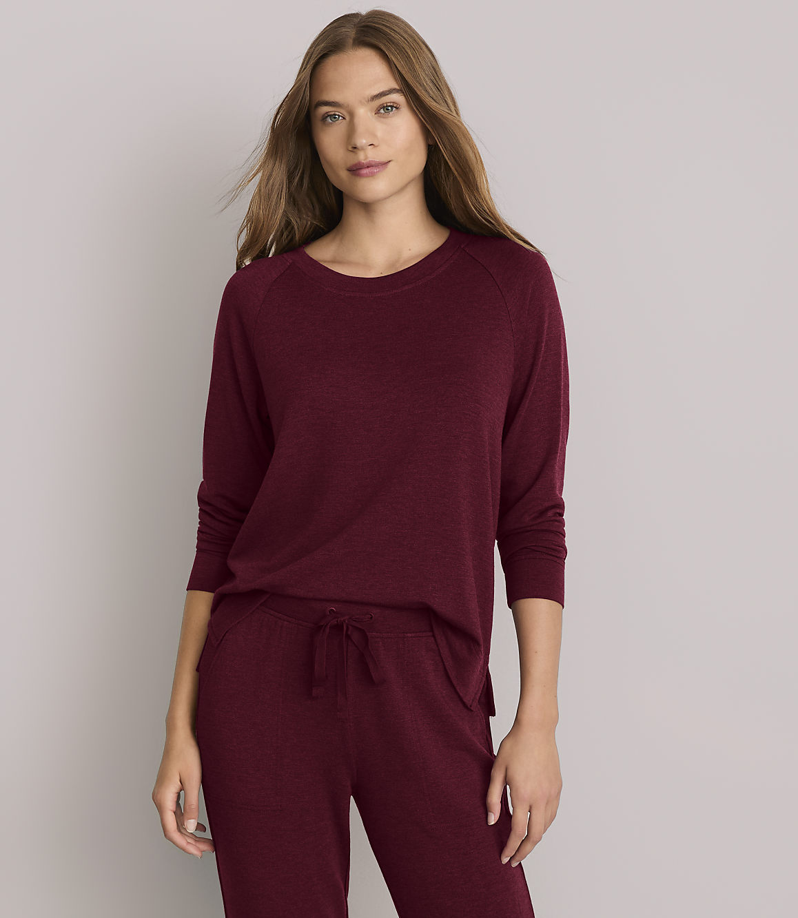 A woman in a burgundy loungewear set stands against a plain white background.
