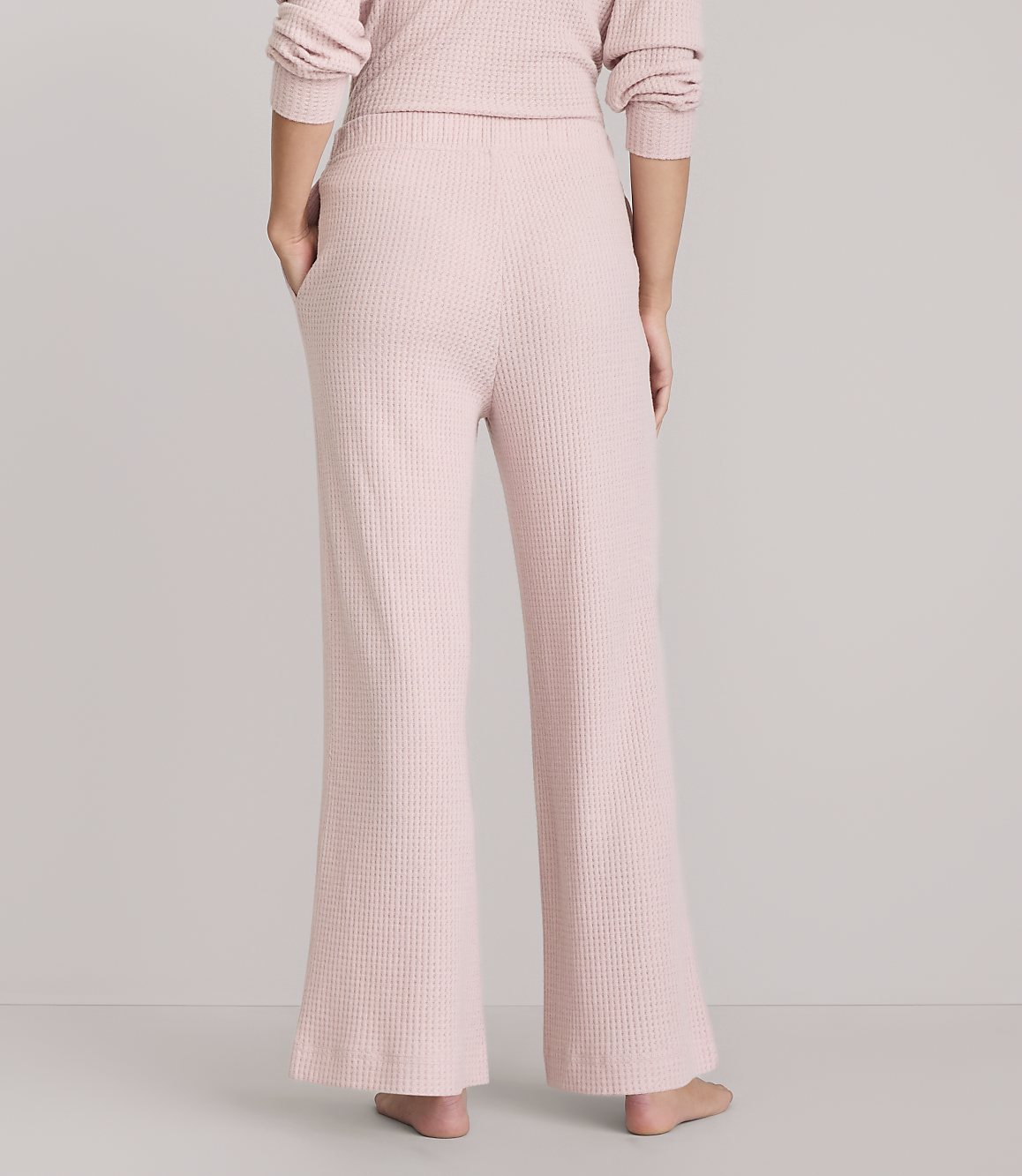 A person wearing pink waffle-knit pajama pants stands against a plain white background.