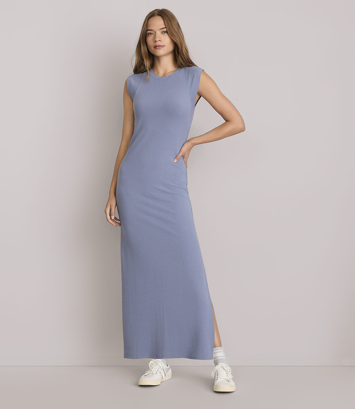 A woman in a blue ribbed maxi dress stands against a plain white background.