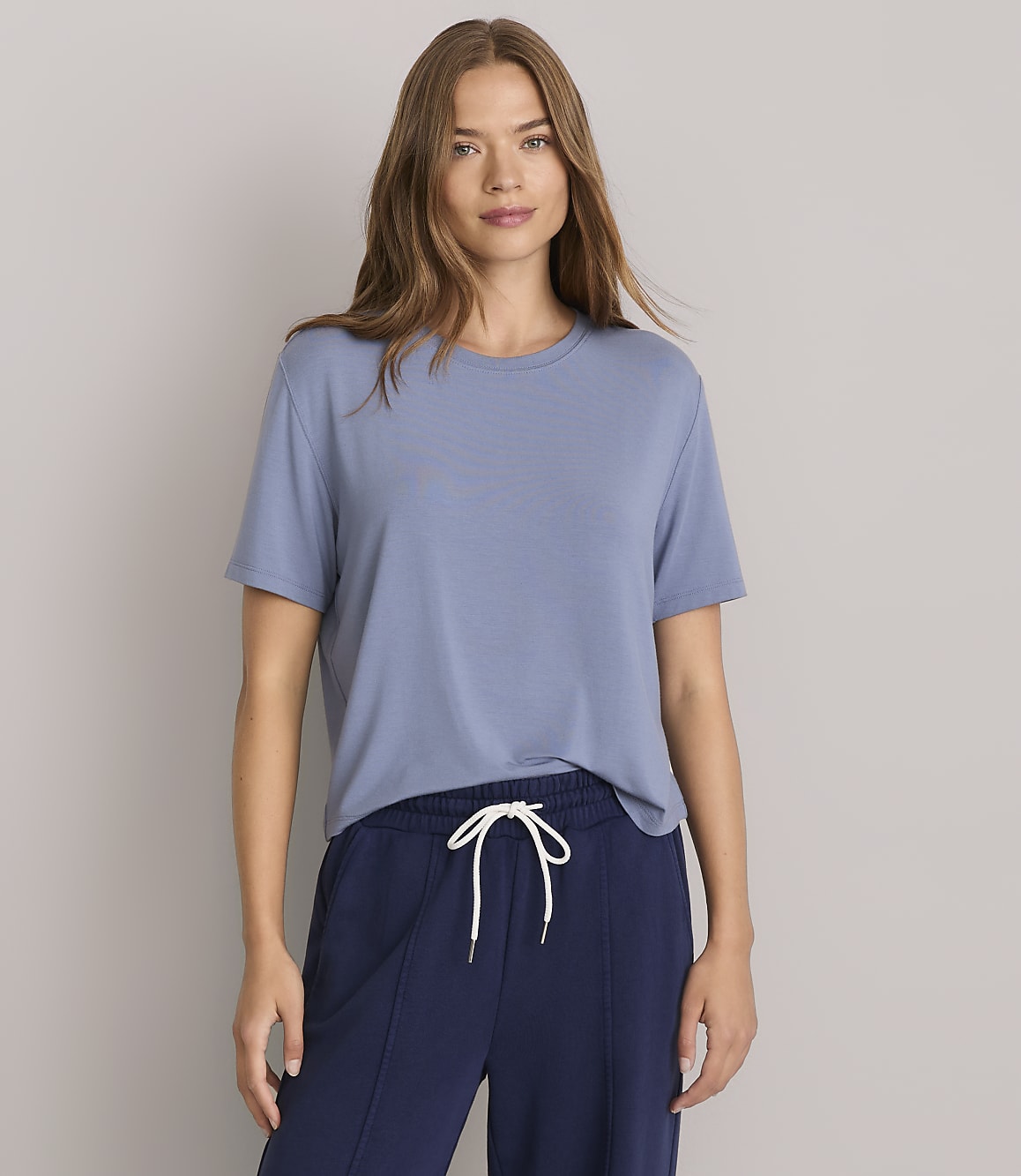 A woman in a blue t-shirt and navy pants stands against a plain gray background.