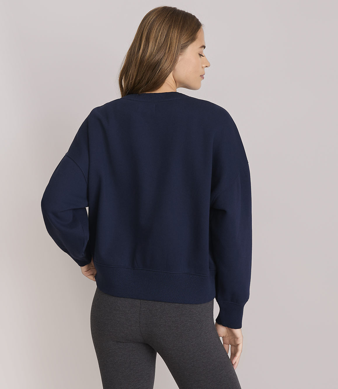 A woman in a navy sweatshirt and grey leggings stands against a plain white background.