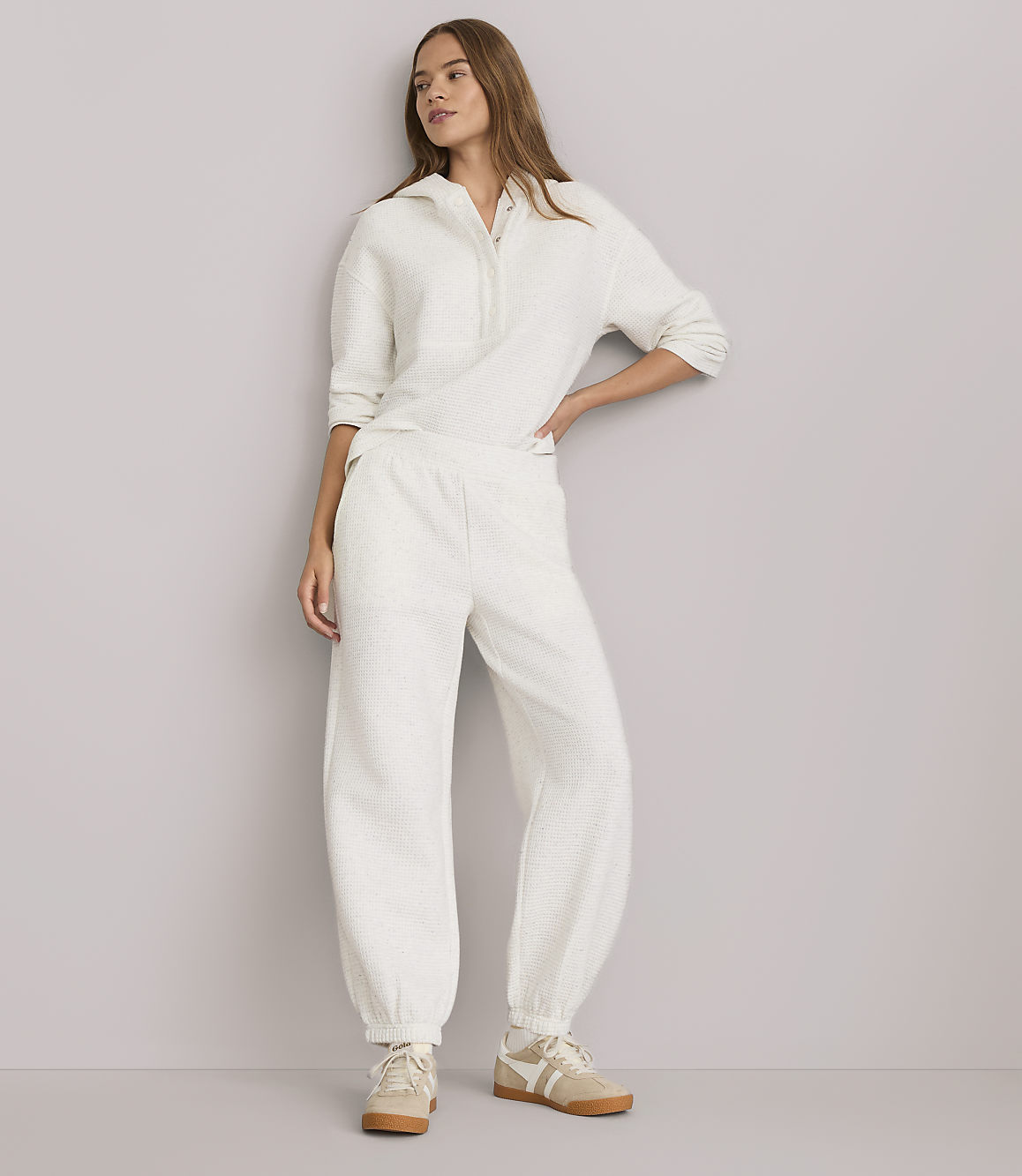A woman in a cream-colored loungewear set stands against a plain gray background.