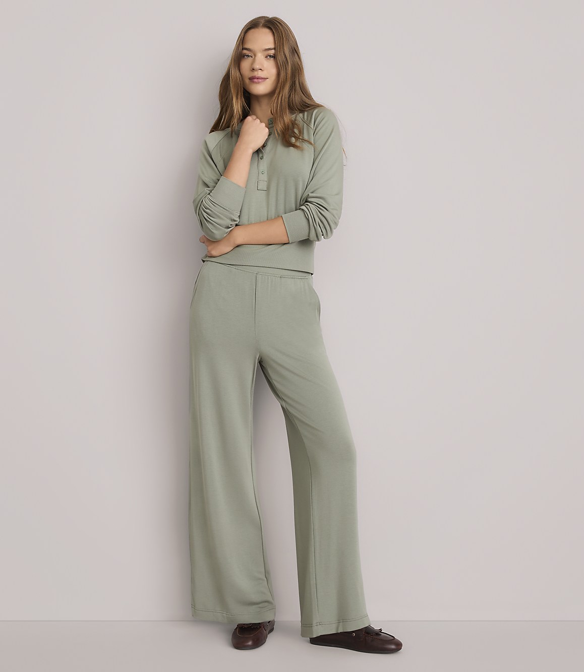 A young woman in a sage green loungewear set stands against a plain white background.