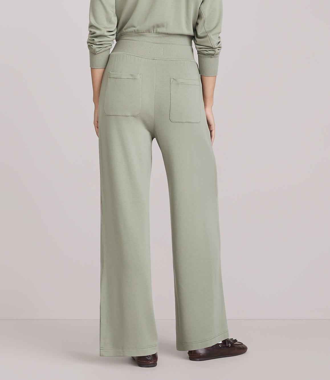 A person wearing light green wide-leg pants and brown loafers stands against a plain white background.