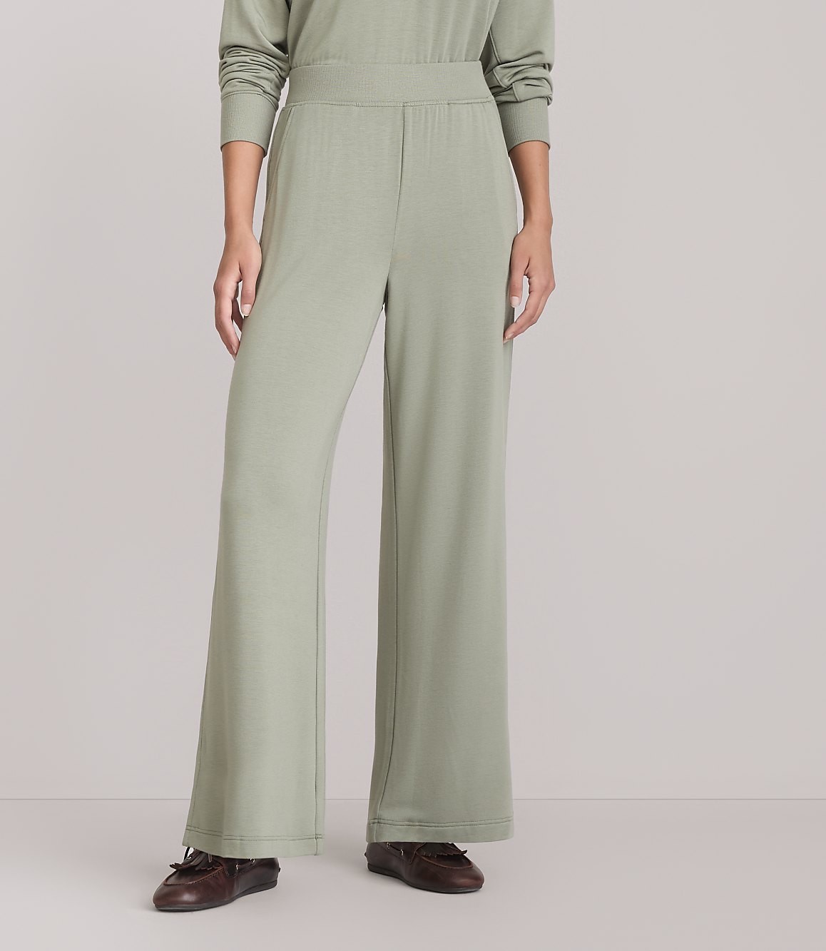 A person wearing light green wide-leg pants and brown loafers stands against a plain white background.