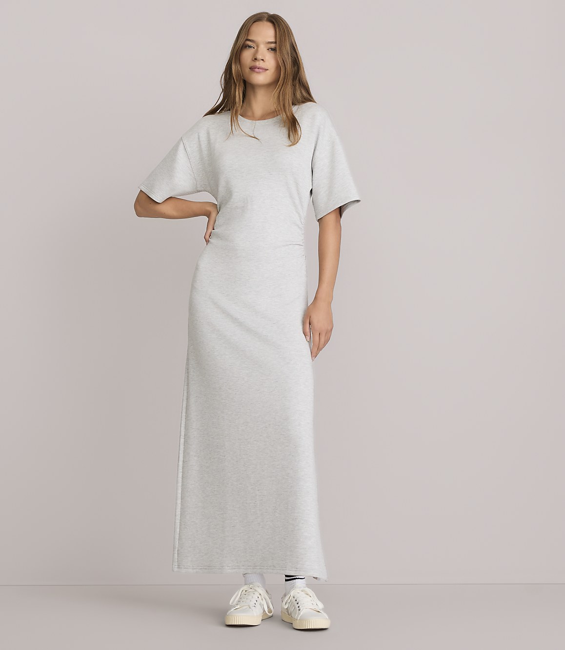A woman in a light gray maxi t-shirt dress stands against a plain white background.