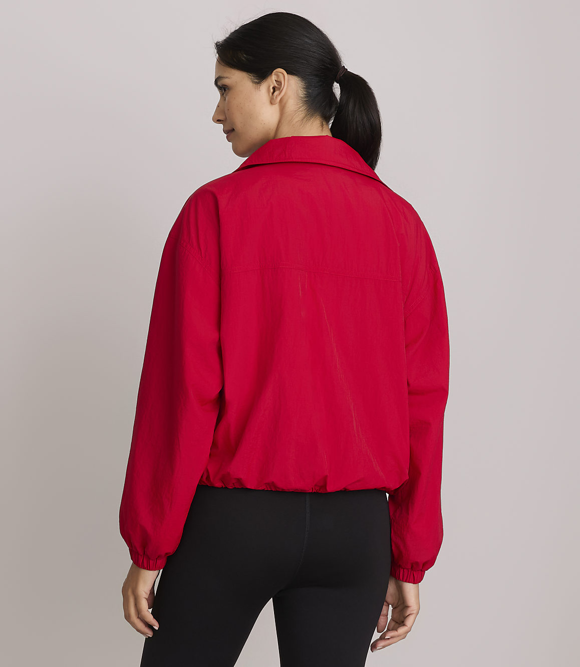 A woman in a red jacket and black leggings stands against a plain gray background.