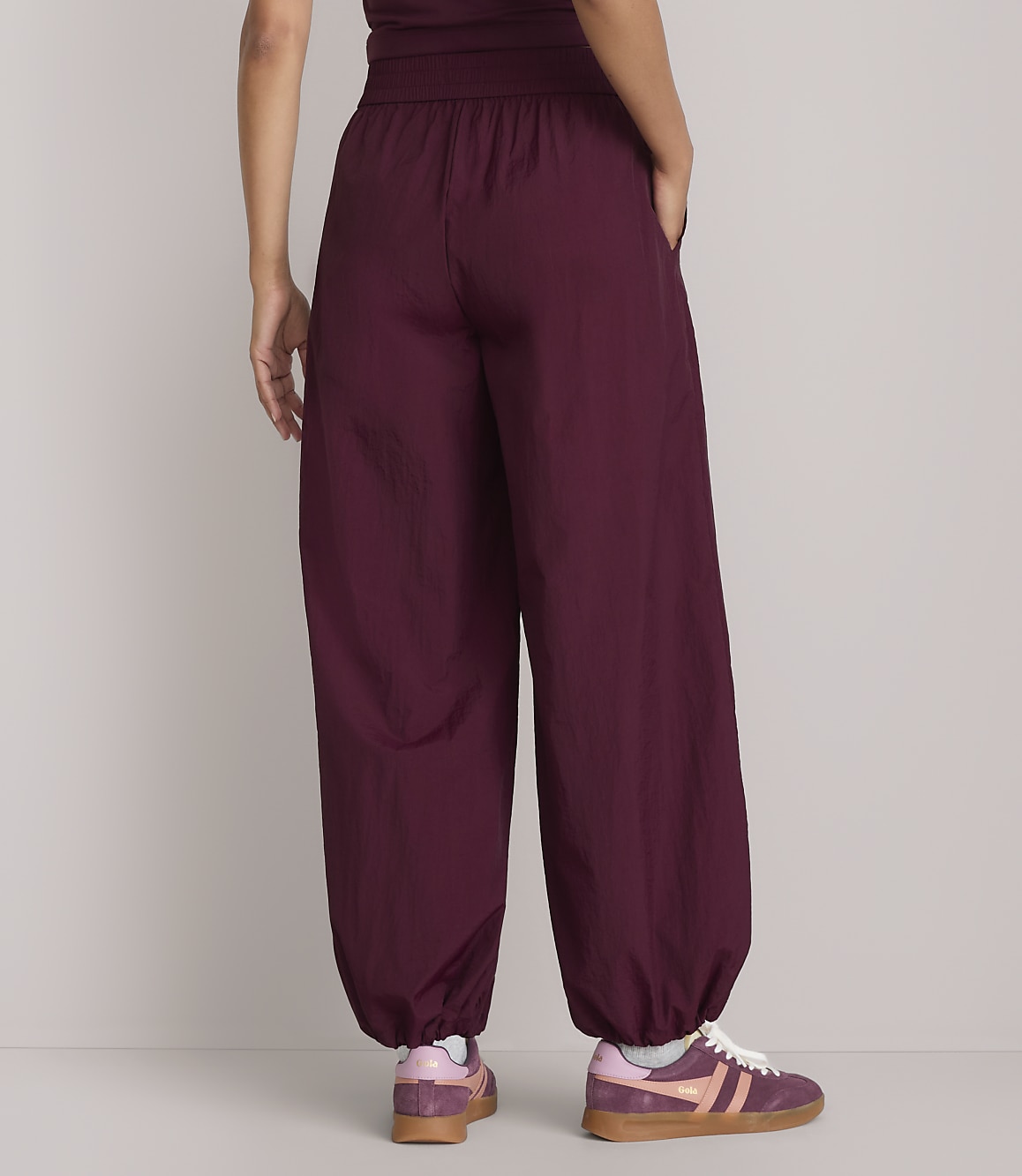A person wearing loose-fitting burgundy pants and sneakers stands against a plain, light-colored background.