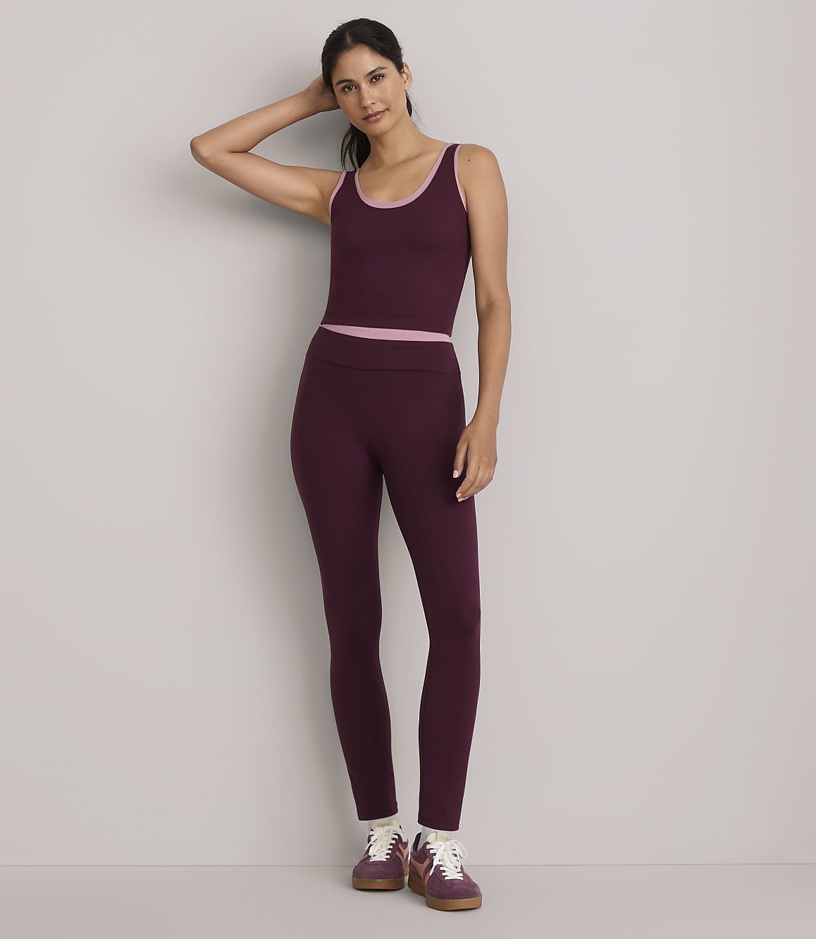 A woman in a burgundy athletic set stands against a plain gray background.