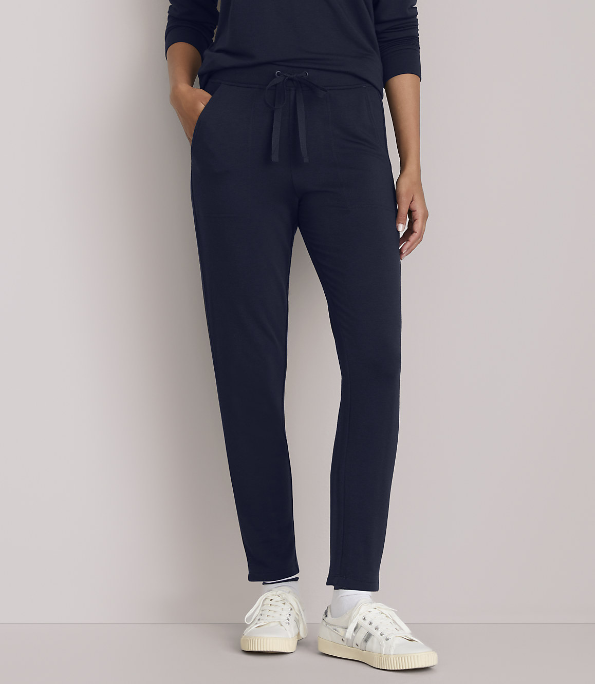 A person in navy blue loungewear and white sneakers stands against a plain, light gray background.