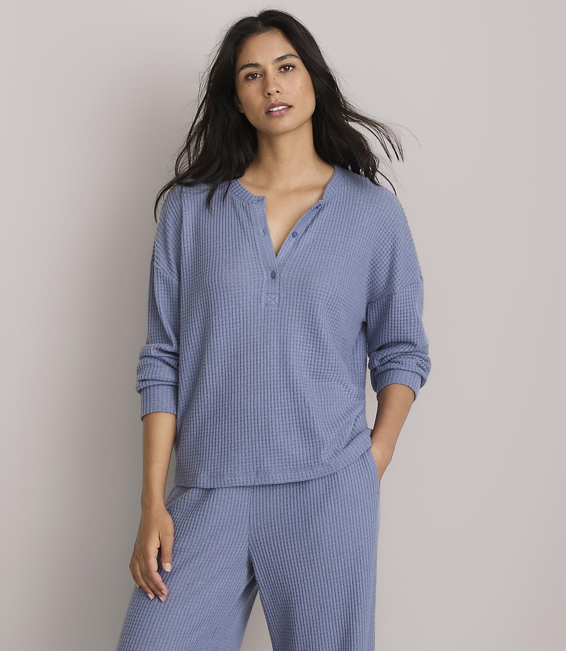 A woman in a blue waffle-knit top and pants stands against a plain gray background.