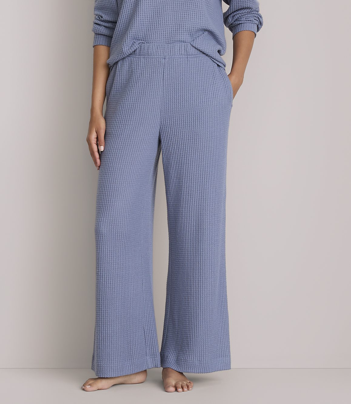 A person stands in blue waffle-knit wide-leg pants and a matching top against a plain gray background.