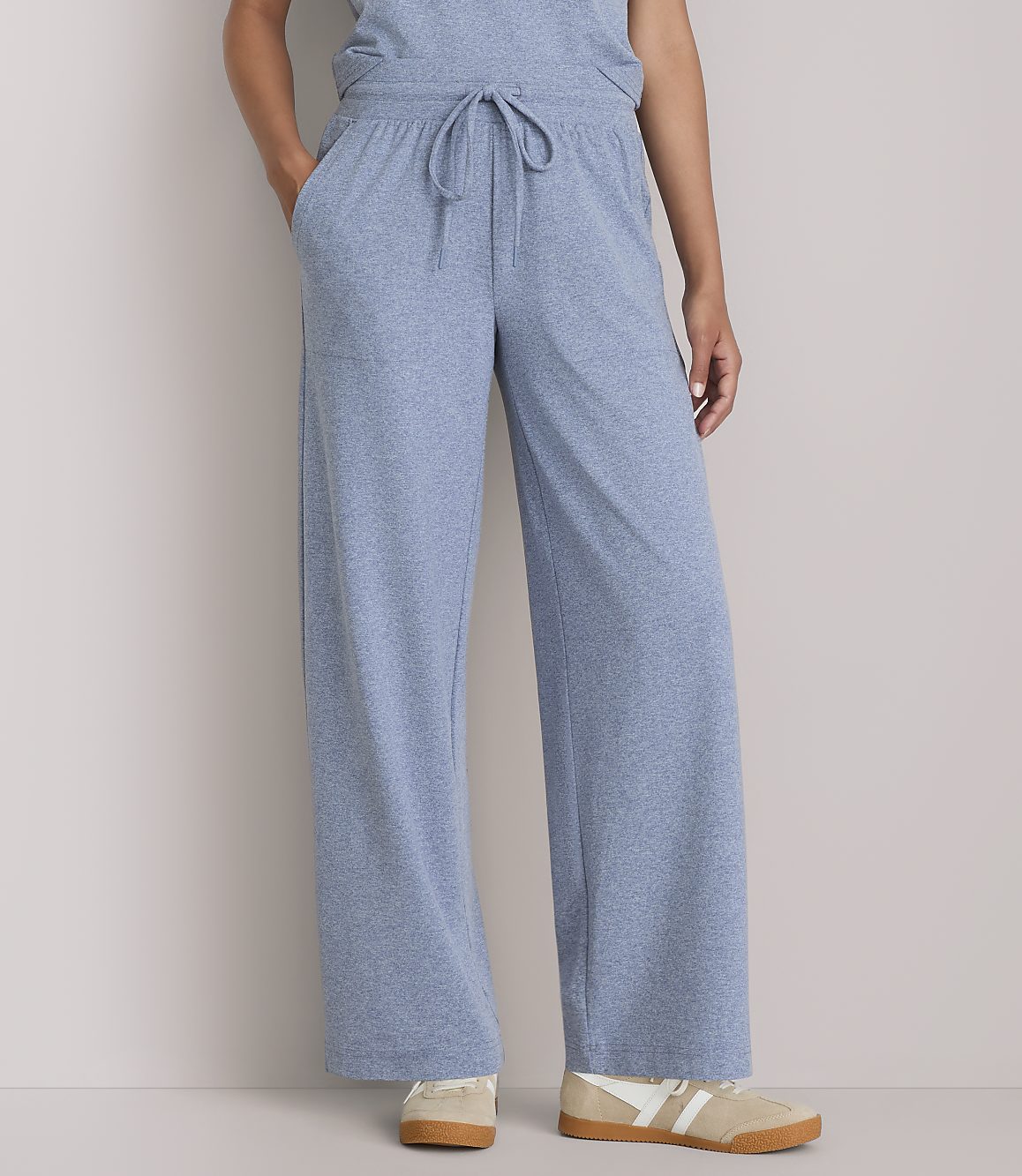 A person stands in light blue wide-leg lounge pants and sneakers against a plain gray background.