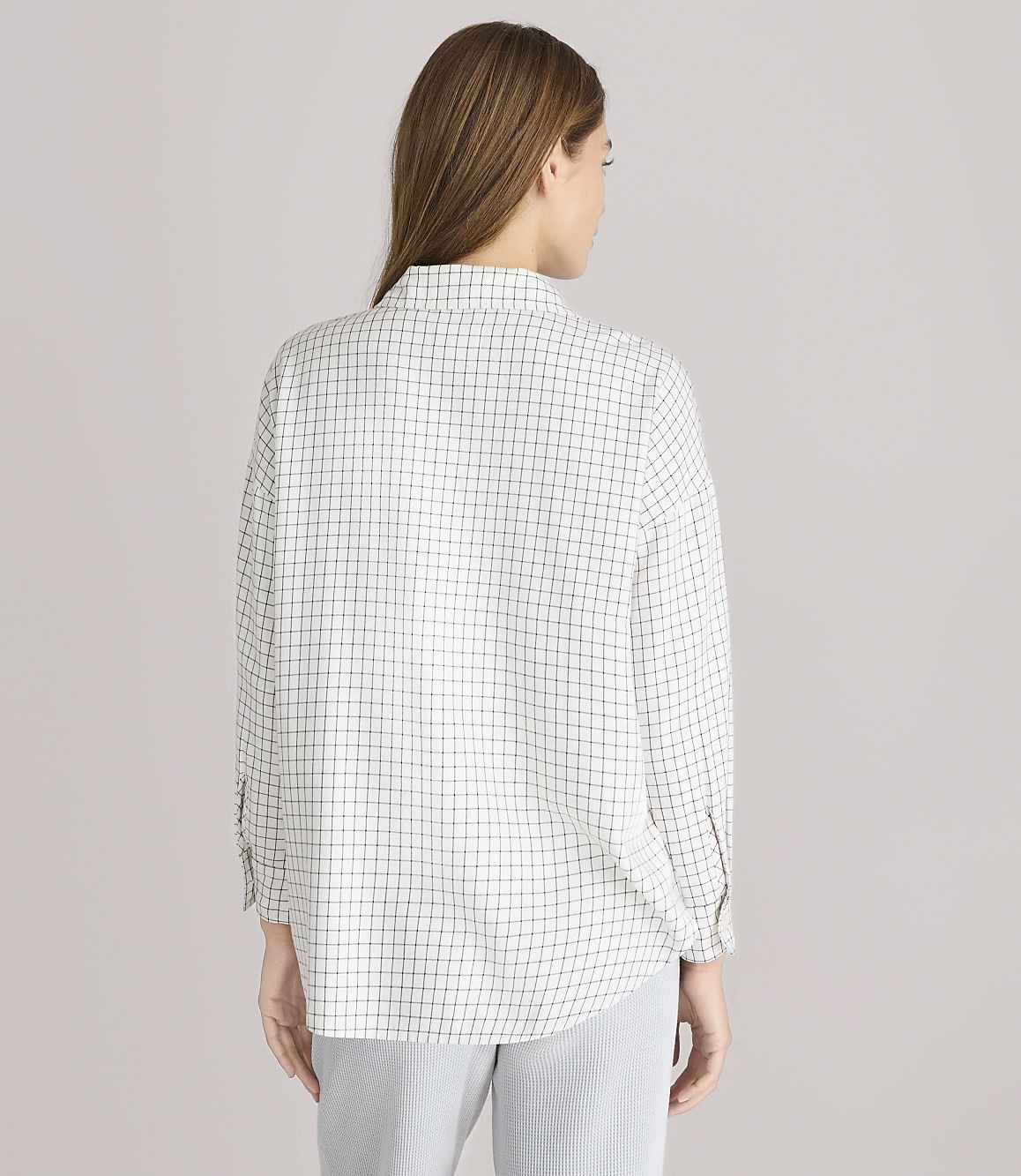 A woman wearing a checkered shirt and striped pants stands against a plain gray background.