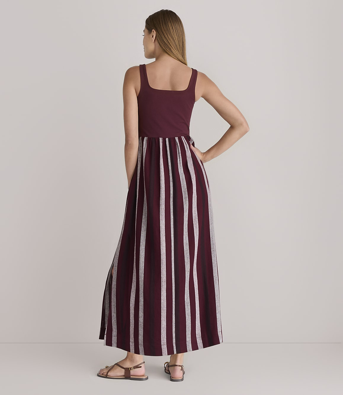 A woman in a maroon and white striped maxi dress stands against a plain white background.