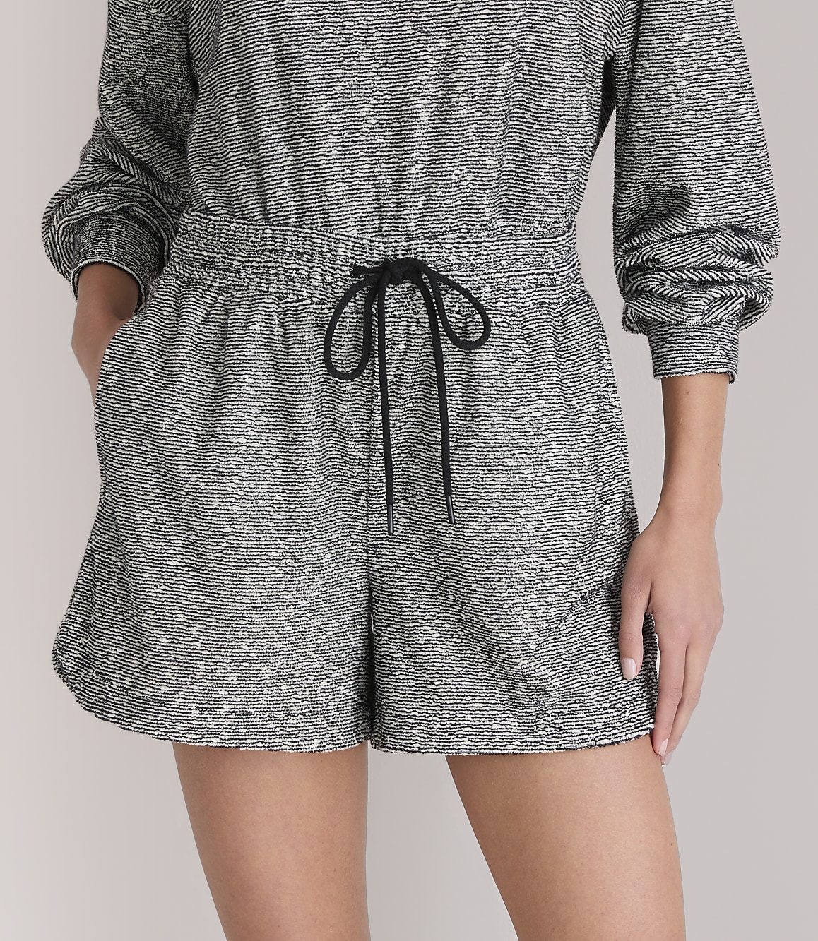A person models a grey and white patterned romper with a black drawstring in the foreground, against a plain white background.