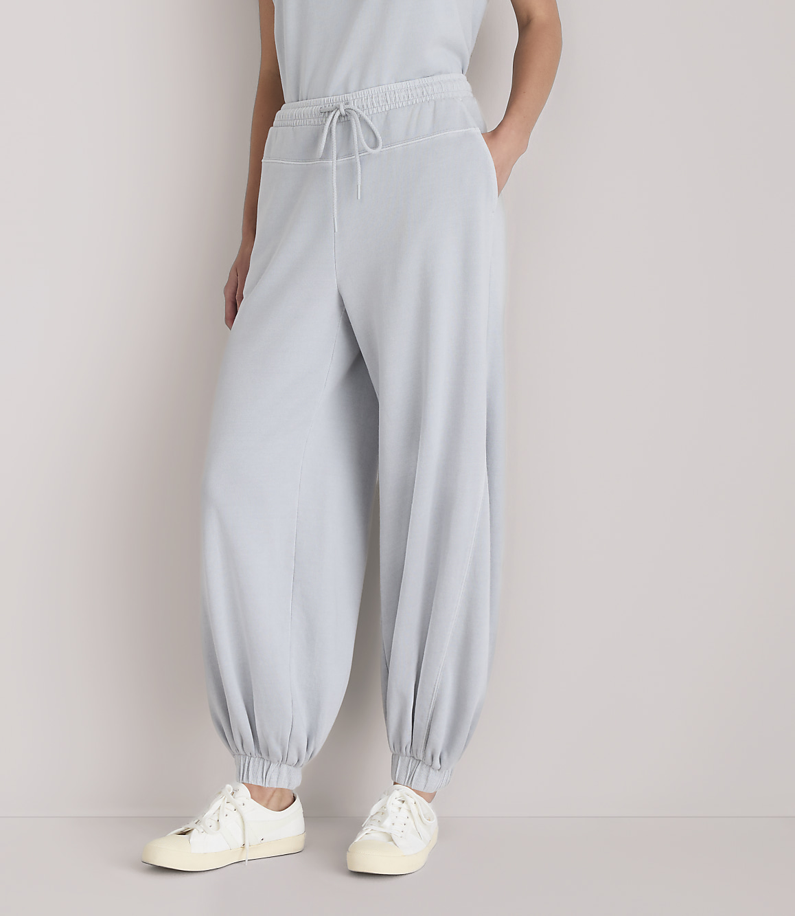 A person stands in light gray, baggy pants and white sneakers against a plain white background.