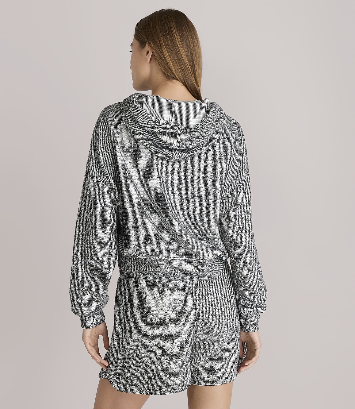 A woman in a sparkly grey hoodie and shorts stands against a plain white background.