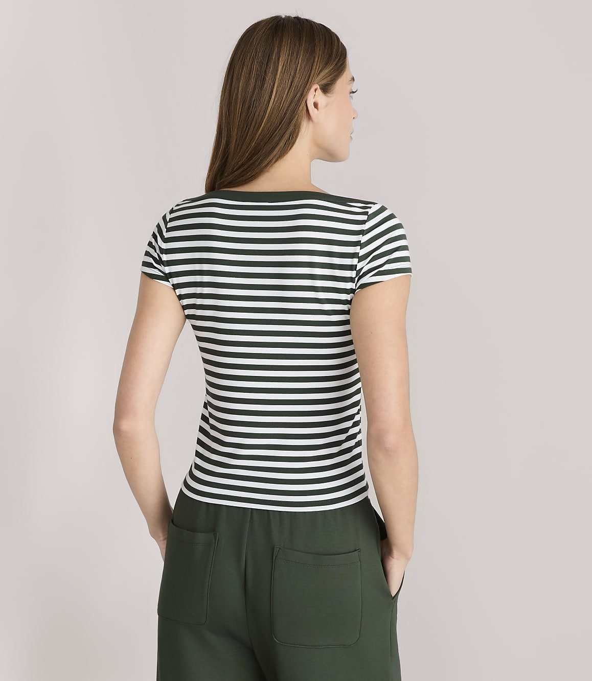 A woman in a striped t-shirt and green pants stands against a plain gray background.
