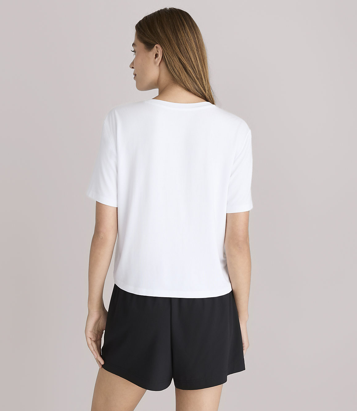 A woman in a white t-shirt and black shorts stands against a plain white background.