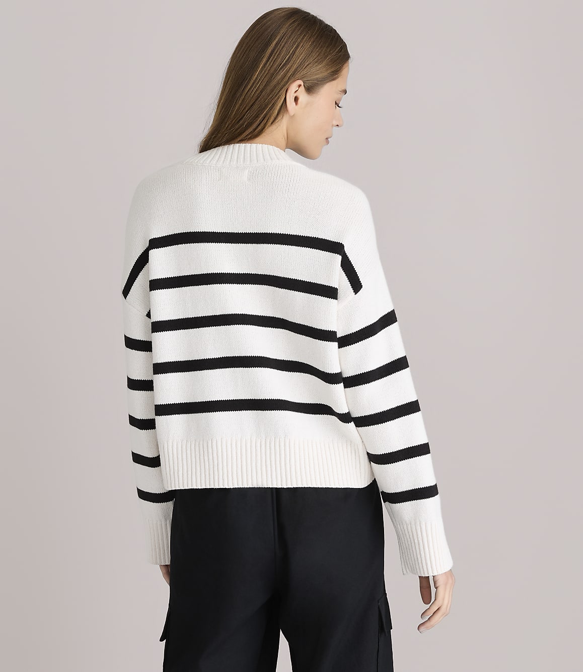 A woman in a white and black striped sweater stands against a plain white background.