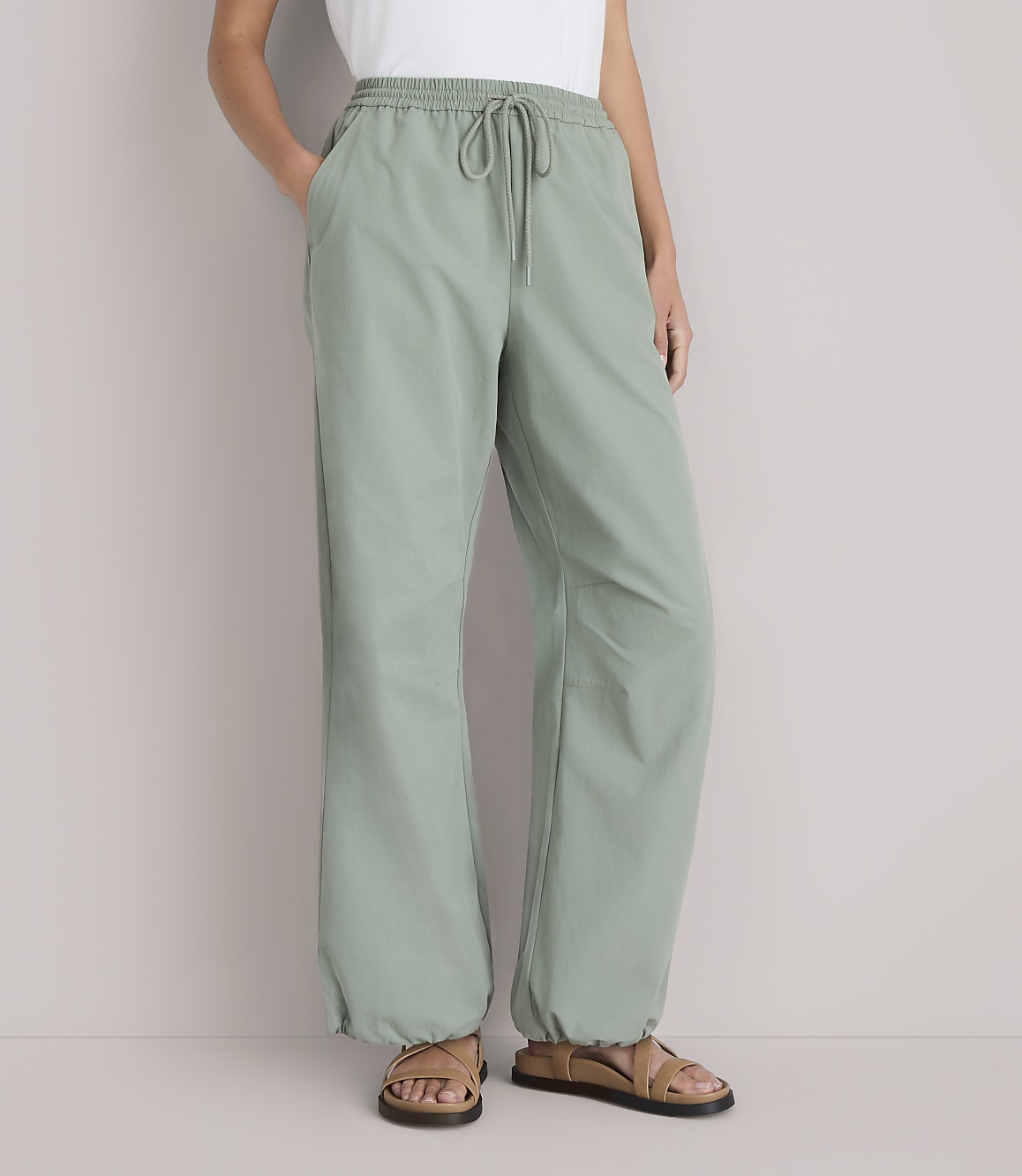 A person stands in light green pants with a drawstring waist and sandals, against a plain white background.