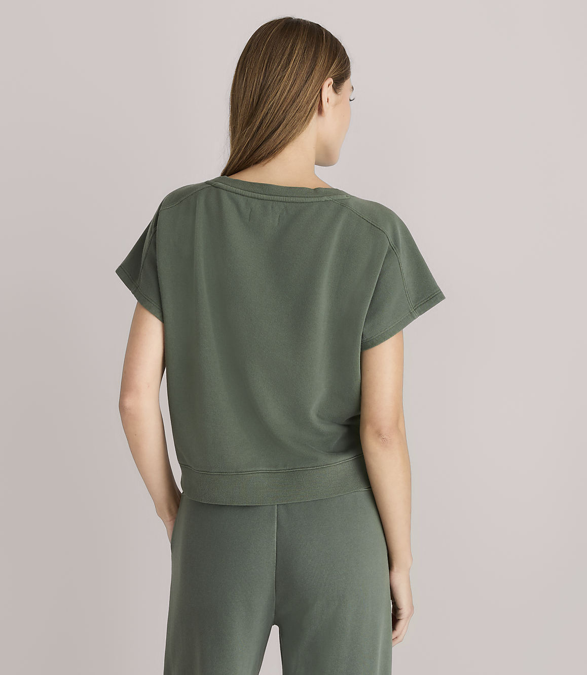 A woman in a green t-shirt and pants stands against a plain gray background.