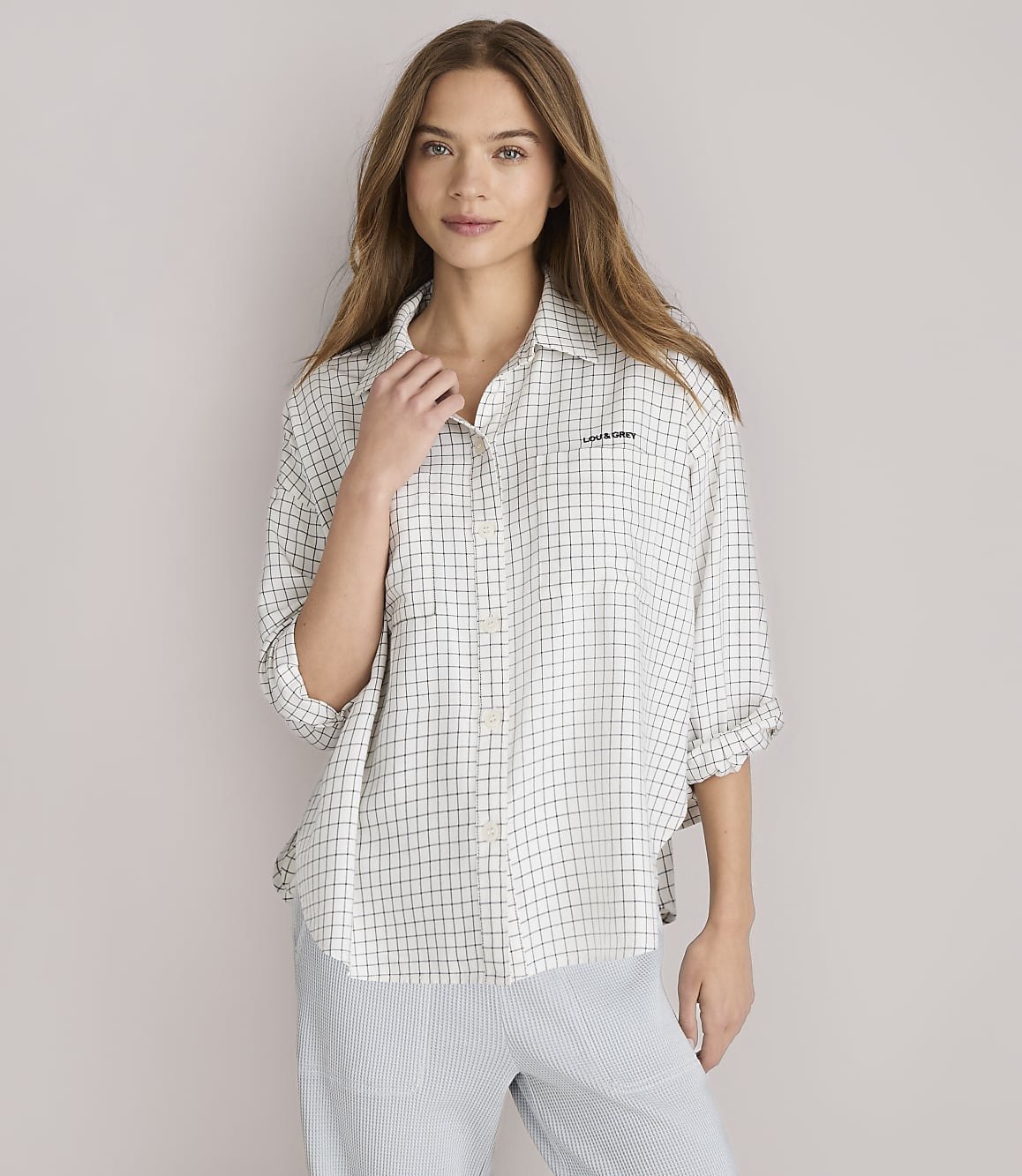 A young woman with long, light brown hair and a checkered shirt is looking forward against a plain white background.