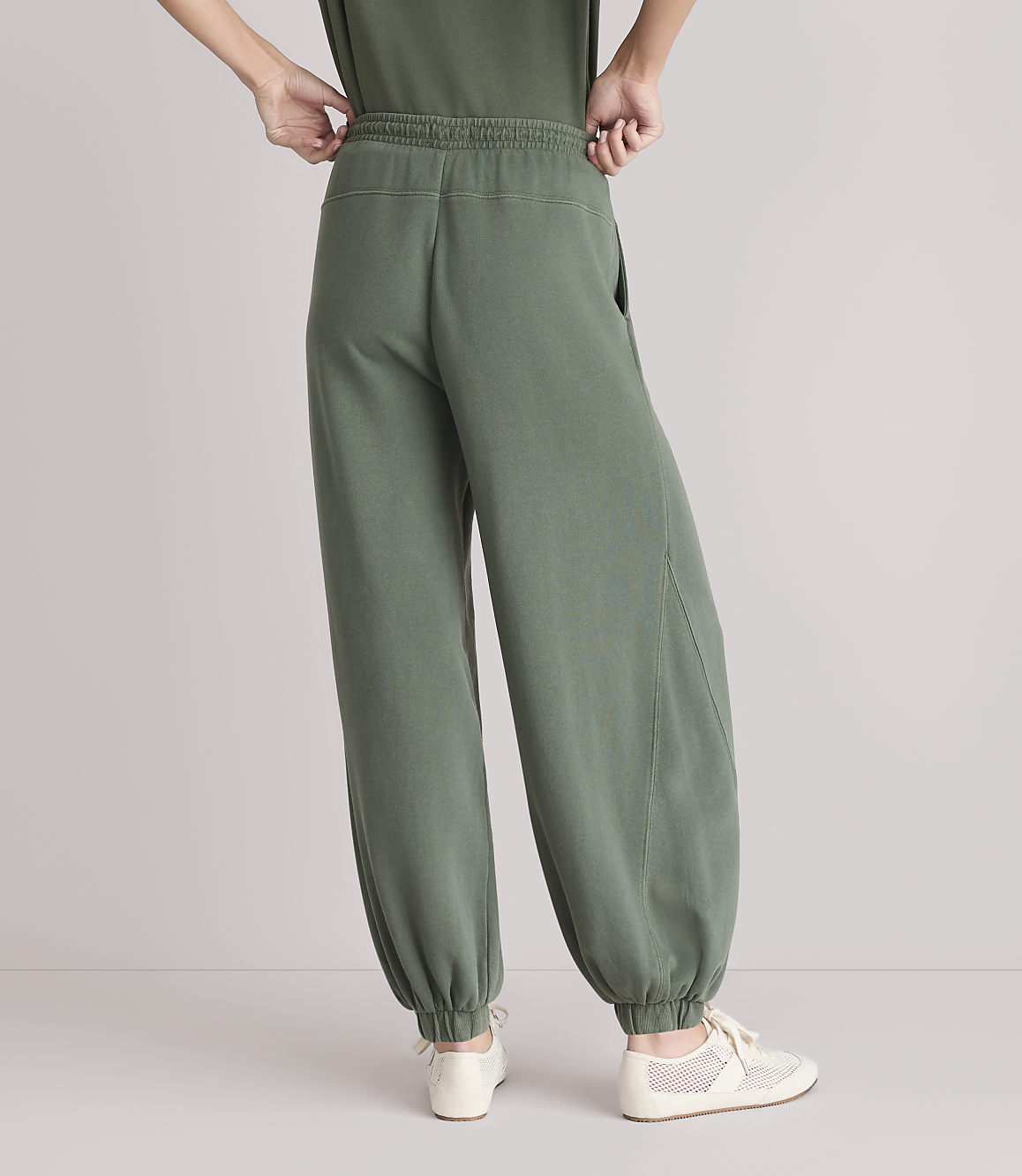 A person wearing loose-fitting green sweatpants and light-colored sneakers stands against a plain white background.