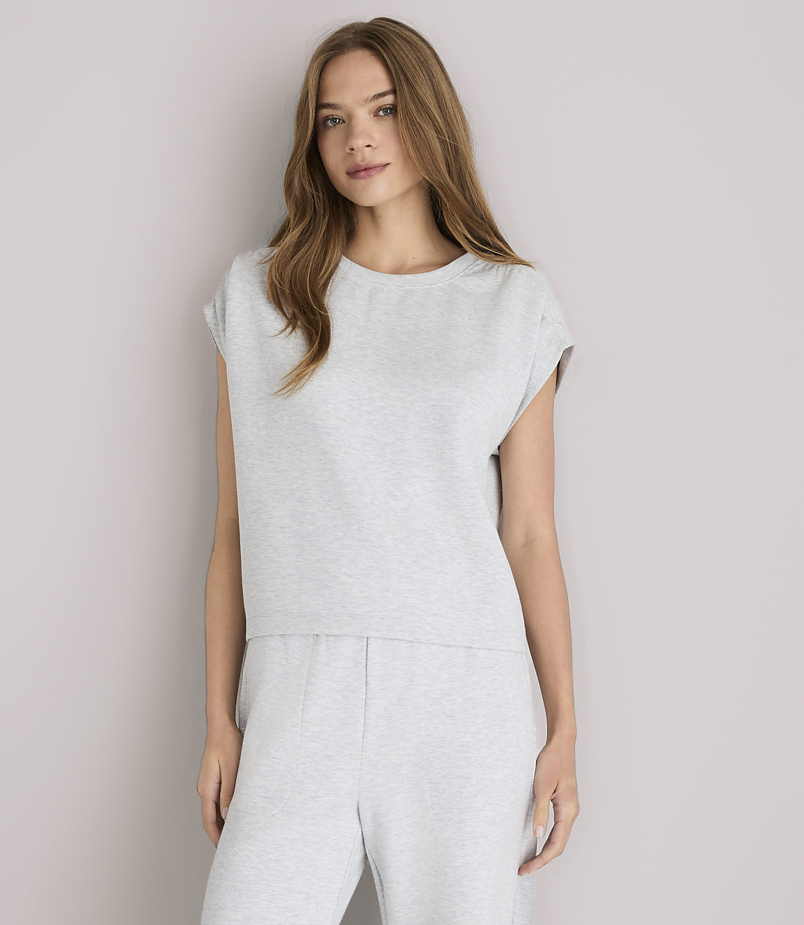 A young woman in a grey loungewear set and white sandals poses against a plain grey background.