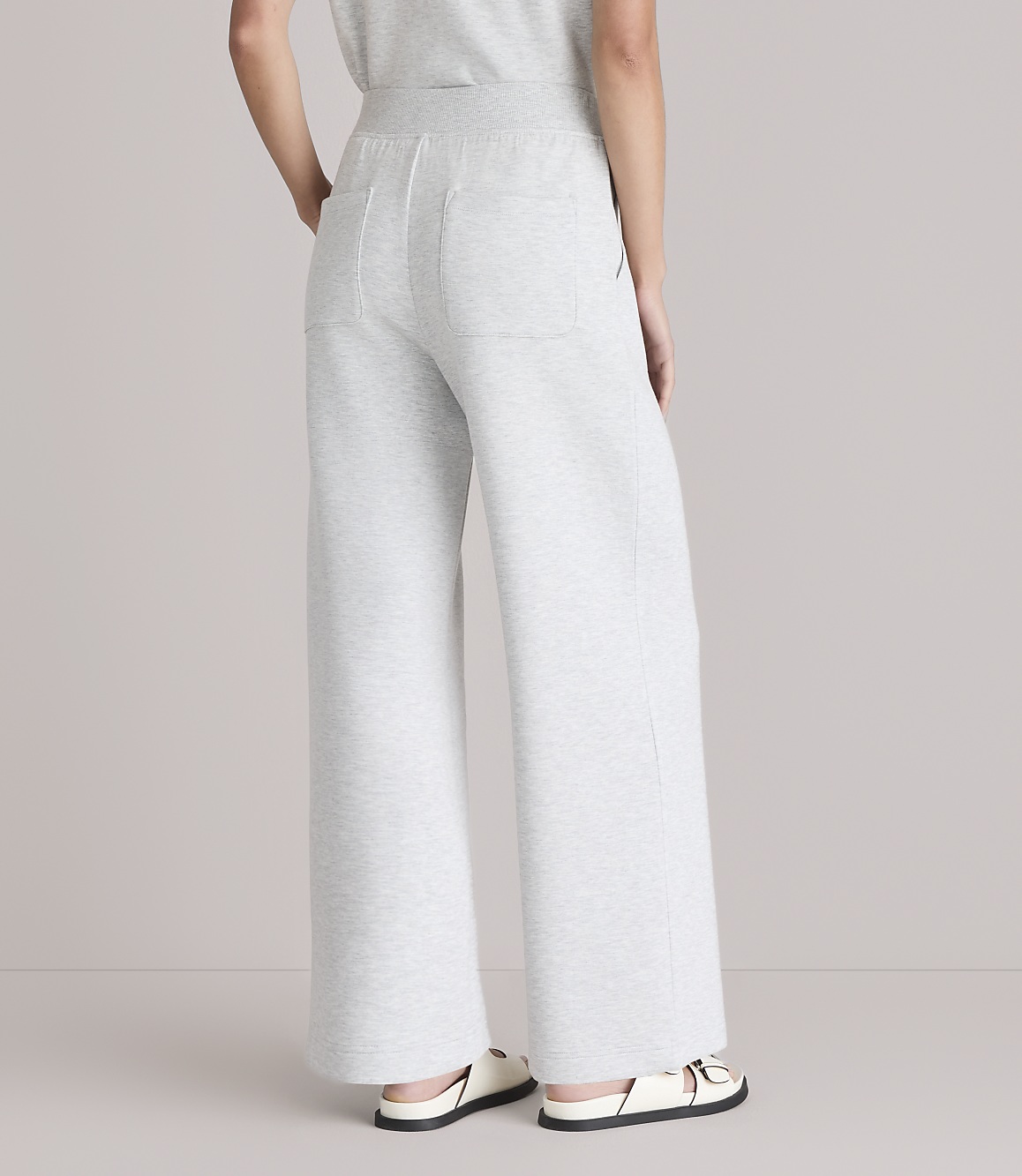 A person wearing light gray wide-leg sweatpants and white sandals stands against a plain white background.