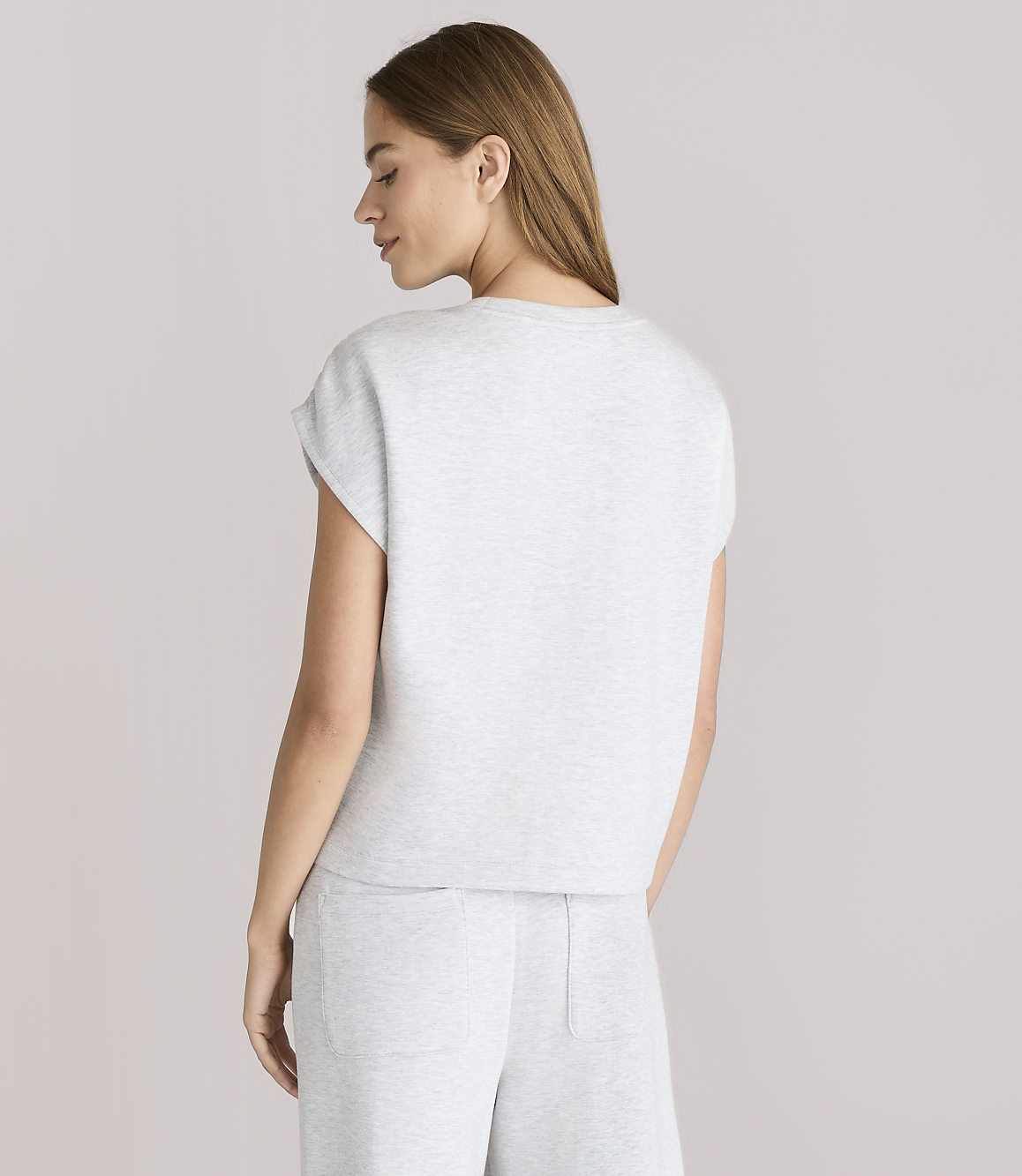 A woman in a light gray t-shirt and pants stands against a plain white background.