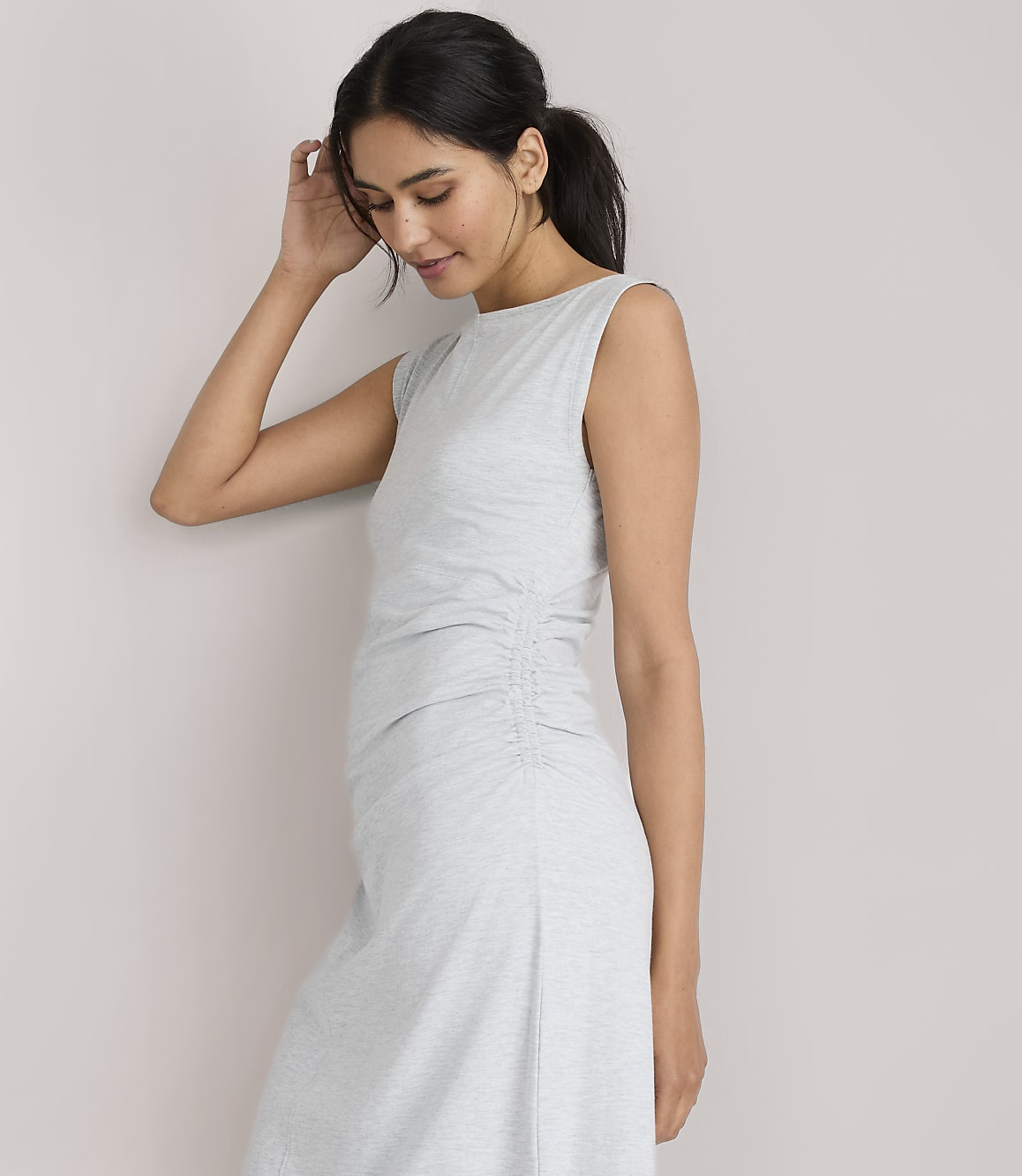 A woman in a light gray ruched dress stands against a plain white background.