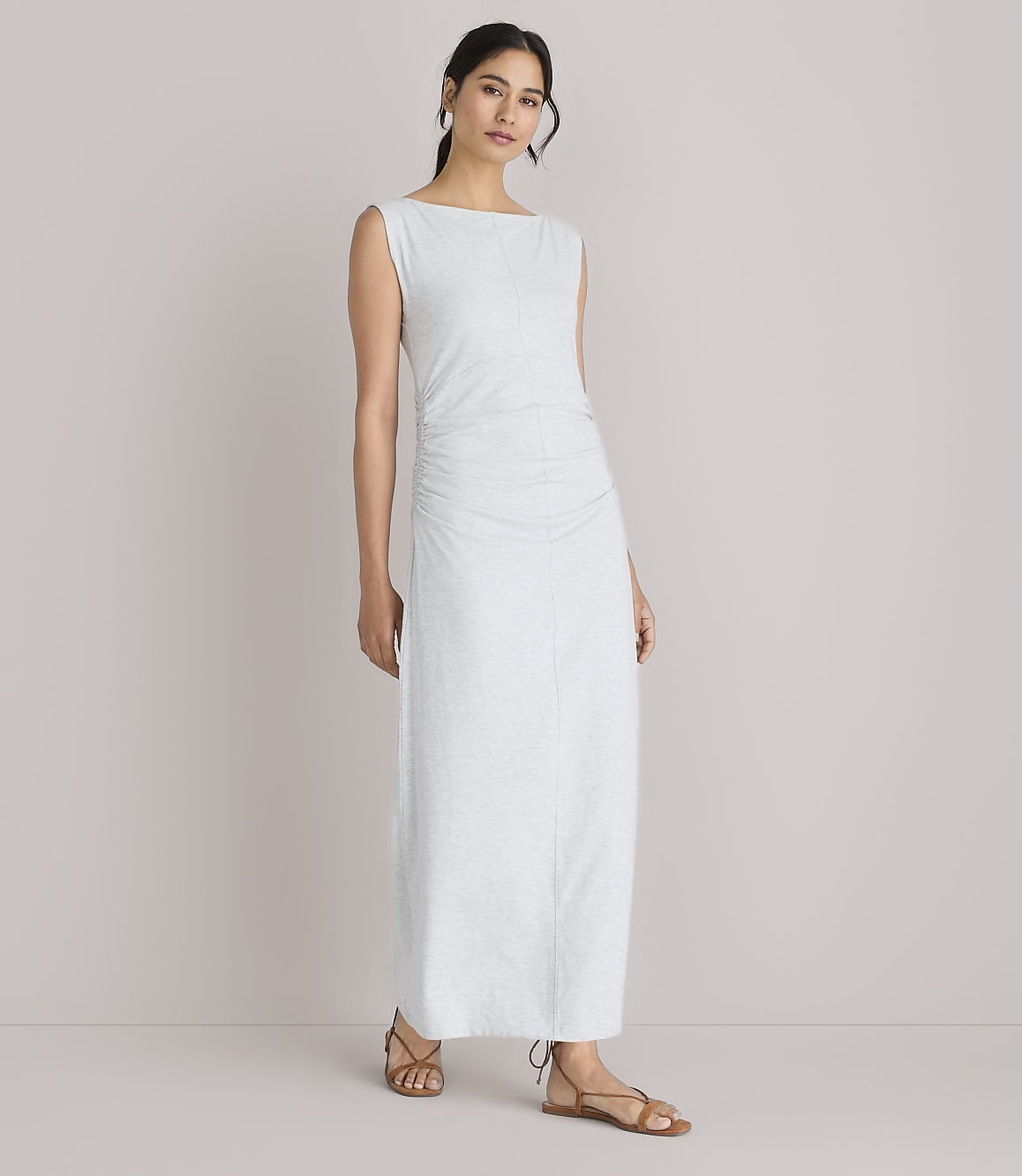A woman in a light-colored, ruched maxi dress stands against a plain white background.