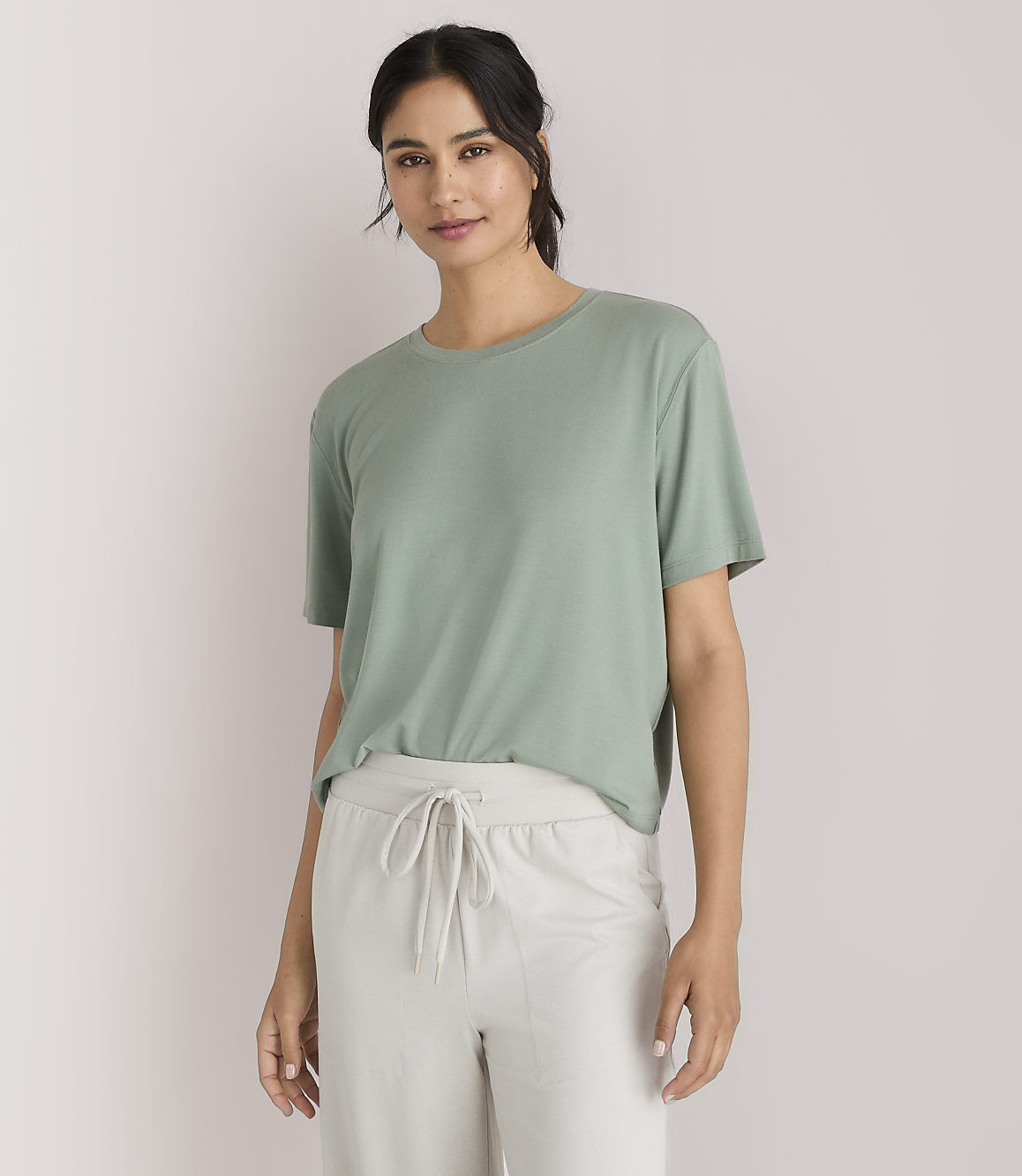 A woman in a green t-shirt and light-colored pants stands against a plain white background.