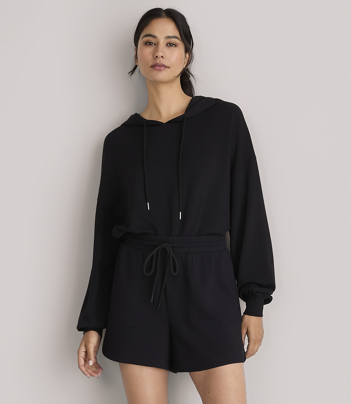 A woman in a black hoodie and shorts stands against a plain white background.